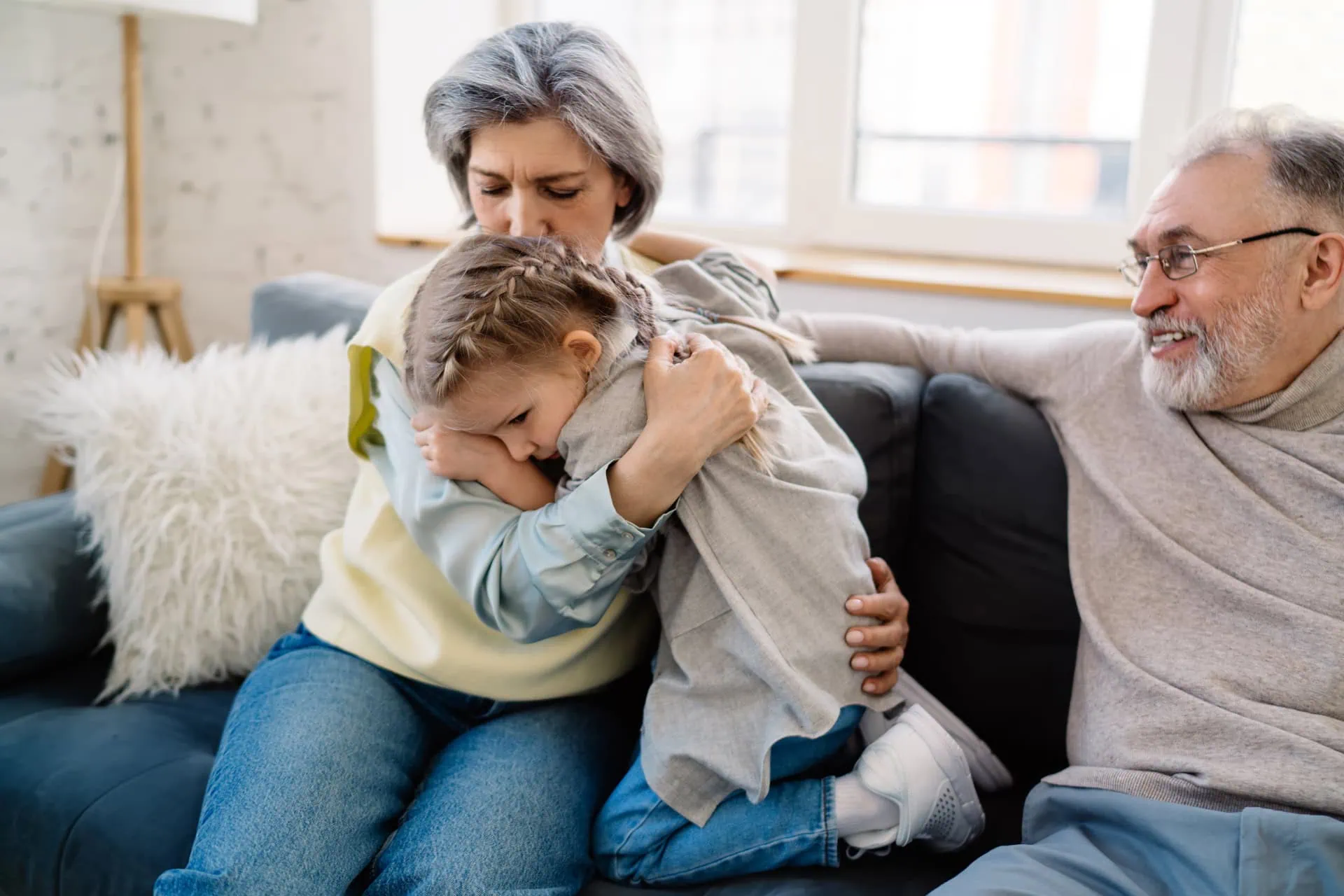 Omas Hausmittel gegen Husten - Oma mit kranken Kind im Arm und Opa auf der Couch, Kind mit Husten